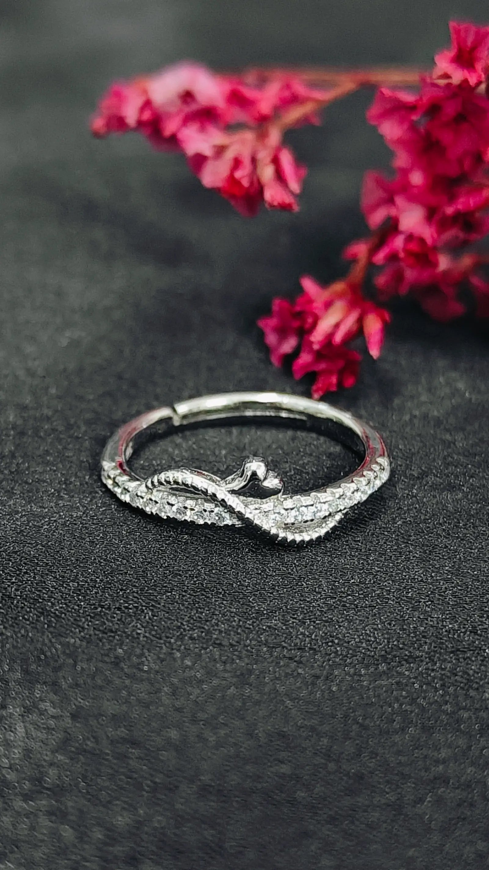 Silver ring with intricate design on a dark surface with pink flowers in the background